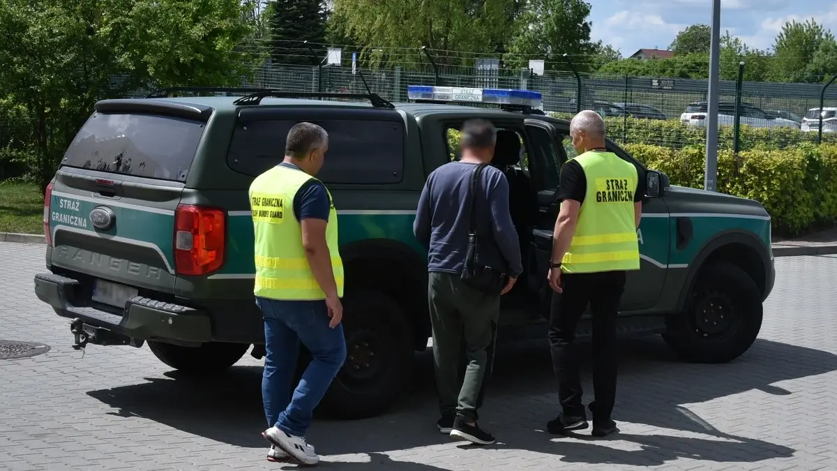 Border Guard officers escort a man toward a service vehicle