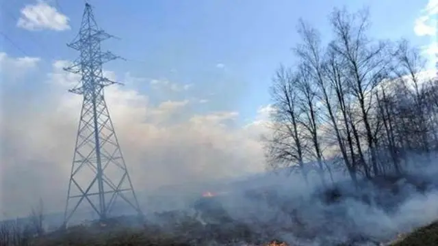 A grass fire beneath a high-voltage electricity transmission pylon