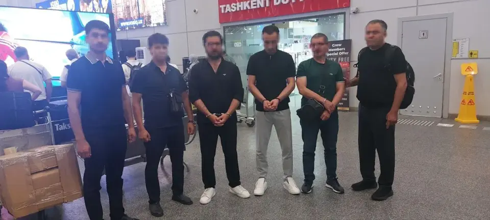 Three extradited men escorted by officers at Tashkent airport